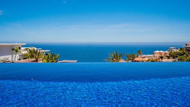 Ein klares, blaues Schwimmbecken mit Blick auf das Meer und Gebäude im Hintergrund.