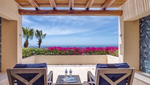 Eine Terrasse mit zwei Holzstühlen, einem kleinen Tisch und Blick auf das Meer.