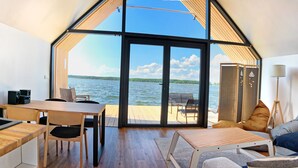 Un interior moderno con cocina, comedor y asientos junto a un gran ventanal con vistas a un lago.