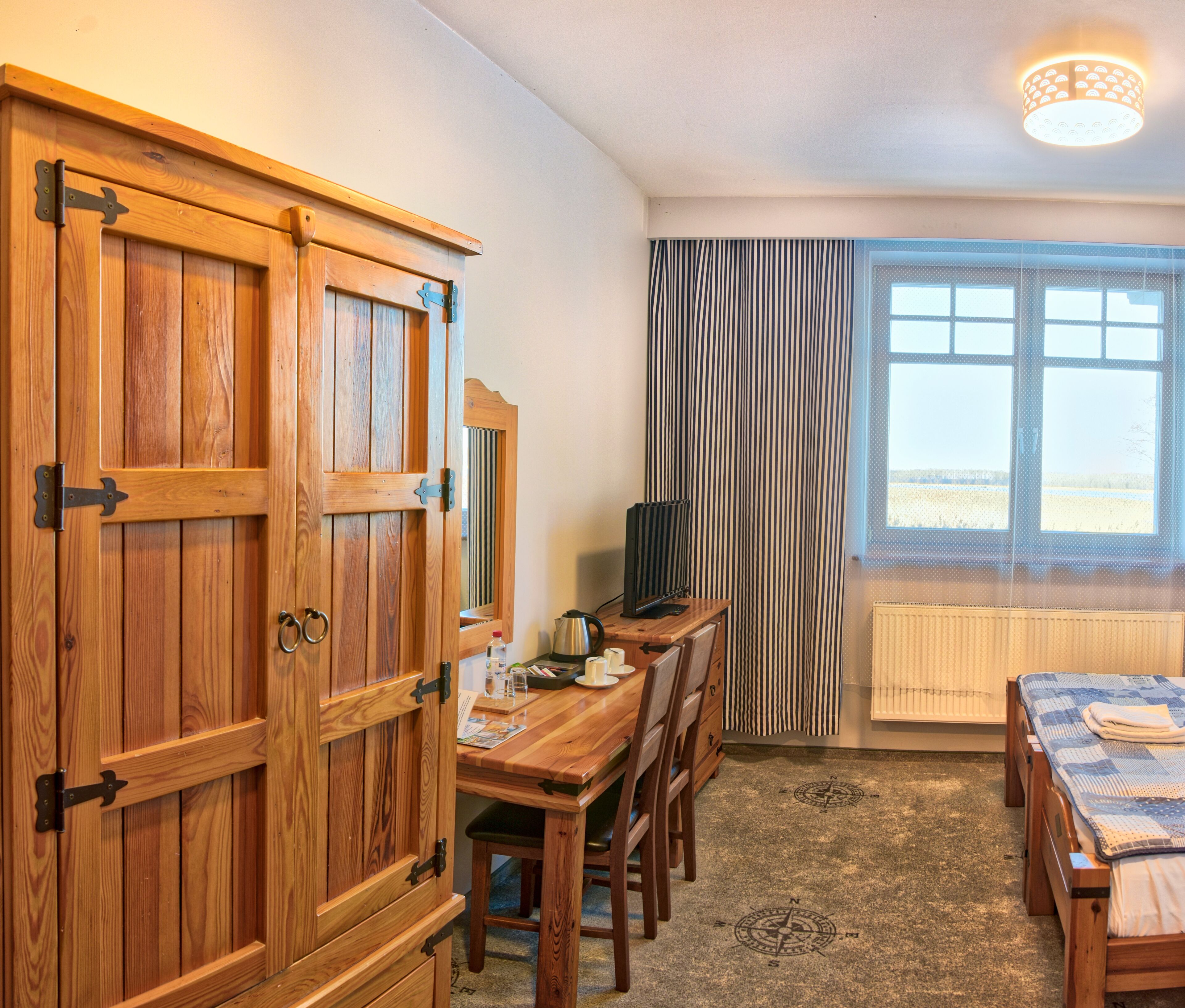 Une pièce comprenant une armoire en bois, une table à manger avec des chaises, un radiateur, une fenêtre avec des rideaux et un luminaire au plafond.