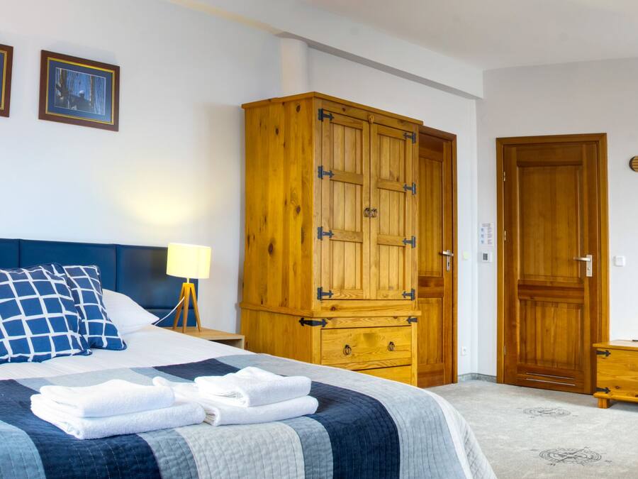 A bedroom with a bed, nightstands, a wooden wardrobe, a wooden chest, and a wooden table.