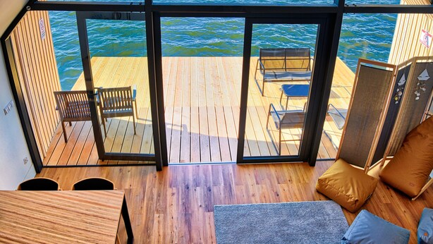 Una habitación amplia con un gran ventanal que da a una terraza de madera con vistas al agua.