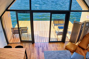A spacious room with a large glass door leading to a wooden deck overlooking the water. - Hotel Joseph Conrad (Pisz)