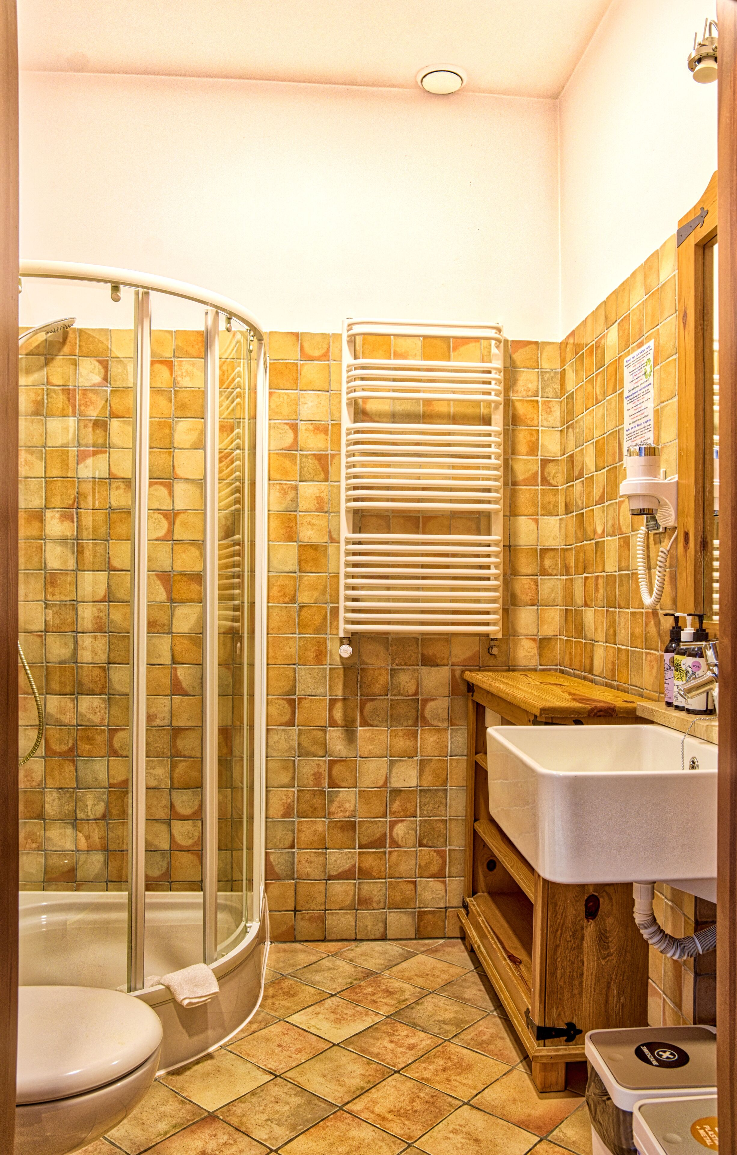 A bathroom with a glass shower enclosure, a white toilet, a wooden vanity with a sink, and a towel rack.
