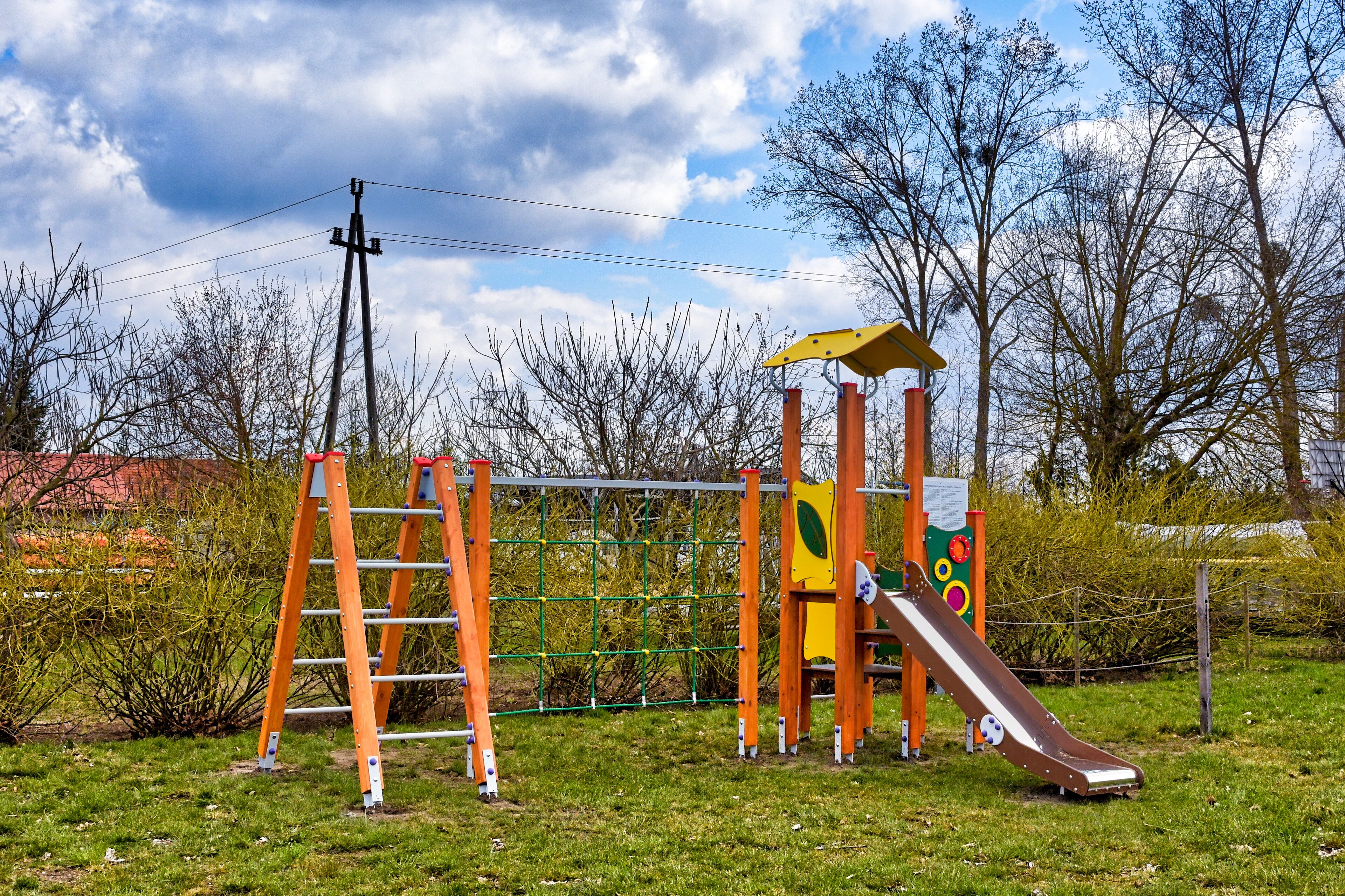 A playground with a slide, climbing net, and a ladder.