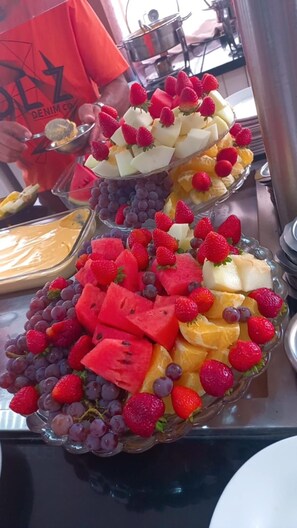 A buffet with various fruits and a person in a red shirt. - Hotel Mirante do Parque (Penha)