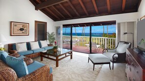 Un vaste espace de vie comprenant un canapé, une table basse et un téléviseur. Un balcon offre une vue sur l’océan.