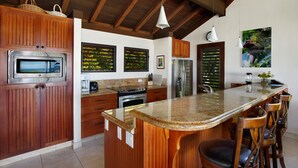 Une cuisine moderne avec des meubles en bois, un plan de travail en granit, des appareils électroménagers en acier inoxydable et un grand îlot central doté de tabourets de bar.