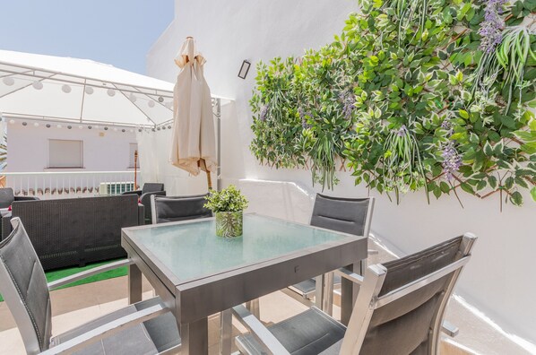A patio with a glass table, chairs, and a potted plant.