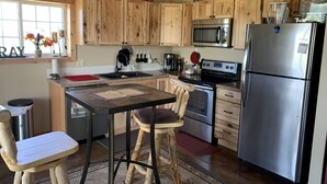 A kitchen with wooden cabinets, a stainless steel refrigerator, a microwave, an oven, and a sink. There is a bar stool and a table with a placemat.