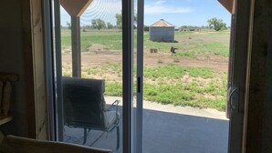 A room with a sliding glass door leading to a covered outdoor area with a metal chair and a small table.