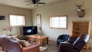 A living room with a brown leather sofa, a blue recliner, a wooden coffee table, a flat-screen TV, and a mounted deer head.