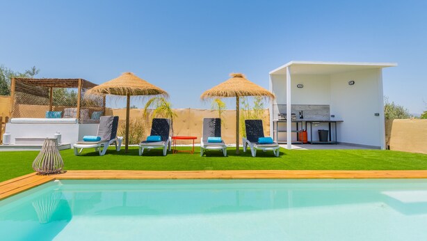 Zona de piscina con sillones de descanso, una barbacoa y un edificio moderno.