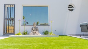 Una estatua de una figura sentada en un jardín, con un ventanal y una puerta al fondo.