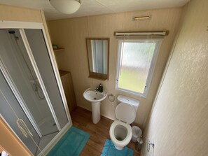 A compact bathroom with a shower, sink, toilet, and a window with a view. - 3 Bed 8 Berth Caravan in California Cliffs - M1 (Great Yarmouth)