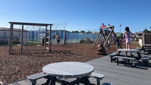 Ein Spielplatz mit einer Holzspielanlage, einem eingezäunten Bereich und Picknicktischen.