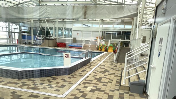 Ein Hallenbad mit Schachbrettmuster auf dem Boden, einem Poolschild und Sicherheitsgeländern.