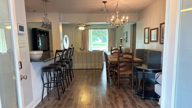 A spacious dining area with a wooden table and chairs, a chandelier, and a view of the outdoors. - Walk to Beach, Casinos & Art – 4BR/4BA with Spacious Covered Porch! (Biloxi)