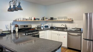A modern kitchen with a granite countertop, stainless steel appliances, and a central island. - Walk to Beach, Casinos & Art – 4BR/4BA with Spacious Covered Porch! (Biloxi)
