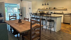 A modern kitchen with a wooden dining table, bar stools, and a built-in island with a sink and microwave. - Walk to Beach, Casinos & Art – 4BR/4BA with Spacious Covered Porch! (Biloxi)