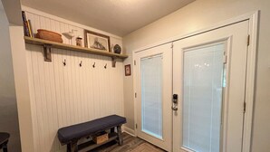 A hallway with a bench, a shelf with decorative items, and two doors with blinds. - Walk to Beach, Casinos & Art – 4BR/4BA with Spacious Covered Porch! (Biloxi)
