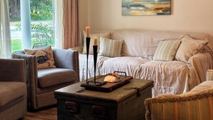 A cozy living room with a sofa, armchair, and a wooden coffee table with candles. - Walk to Beach, Casinos & Art – 4BR/4BA with Spacious Covered Porch! (Biloxi)