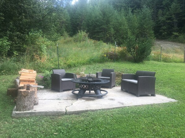 Une terrasse extérieure aménagée avec des meubles en osier, une table ronde et un foyer.