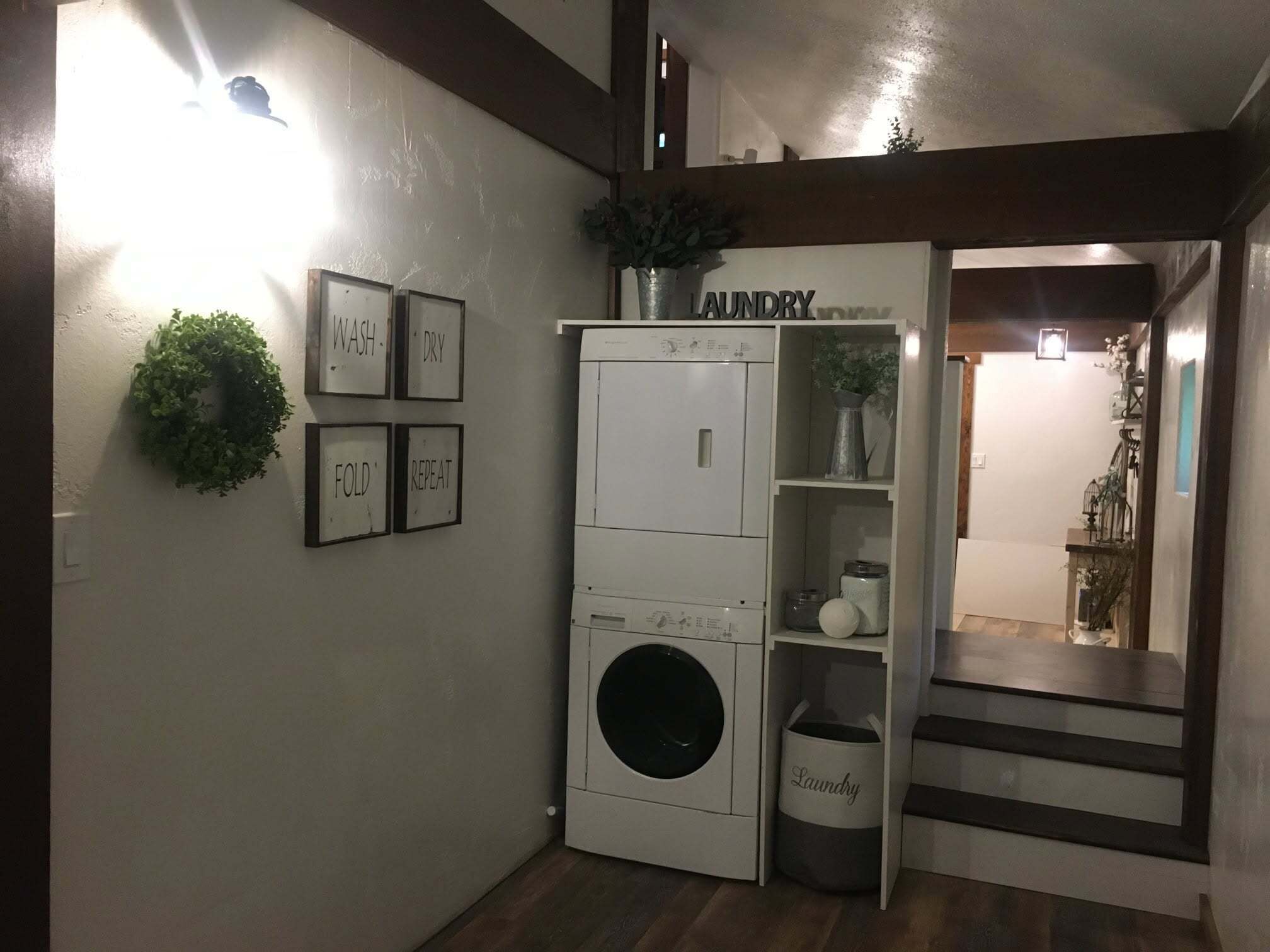 Ein Waschraum mit Waschmaschine und Trockner, ein Regal mit Pflanzen und eine Wand mit eingerahmten Anweisungen.