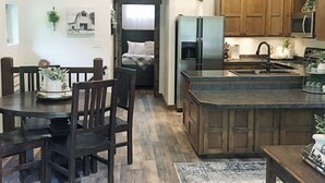 A spacious kitchen with wooden beams, a dining area with dark wooden furniture, and a view into a bedroom. - Get away from the stress and strain of life at this romantic mountain cabin. (Ronan)