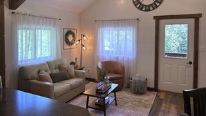 A cozy living room with a sofa, armchair, coffee table, and a wall clock. - Get away from the stress and strain of life at this romantic mountain cabin. (Ronan)