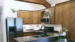 A kitchen with wooden cabinets, a stainless steel refrigerator, a microwave, and a sink with a granite countertop. - Get away from the stress and strain of life at this romantic mountain cabin. (Ronan)