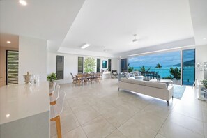 A modern interior with a dining area, a sofa, and a view of the ocean. - Splendeur Sur La Mer (One Bedroom) (Airlie Beach)