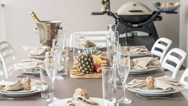Mesa de jantar posta com pratos, talheres, copos e uma abacaxi como peça central.