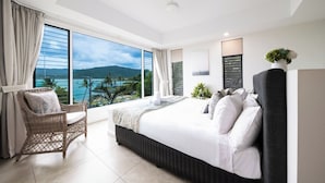 Quarto de hotel com cama grande, cadeira de vime, vista para o mar e varanda.