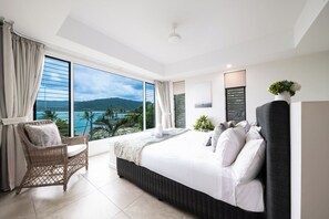 A hotel room with a large bed, a wicker chair, a view of the sea, and a balcony. - Splendeur Sur La Mer (One Bedroom) (Airlie Beach)