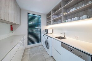A modern kitchen with a built-in washing machine, a microwave, and a shelf with glassware. - Splendeur Sur La Mer (One Bedroom) (Airlie Beach)