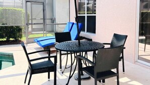 Eine Terrasse mit Tisch, Stühlen und einem blauen Sonnenschirm, sowie ein Schwimmbecken.