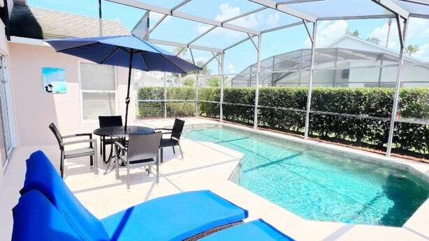 Ein überdachter Außenbereich mit Pool, blauen Liegestühlen und einem Tisch mit Stühlen.