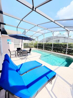 Un espace extérieur abrité comprenant une piscine, des chaises longues bleues et une table avec des chaises.