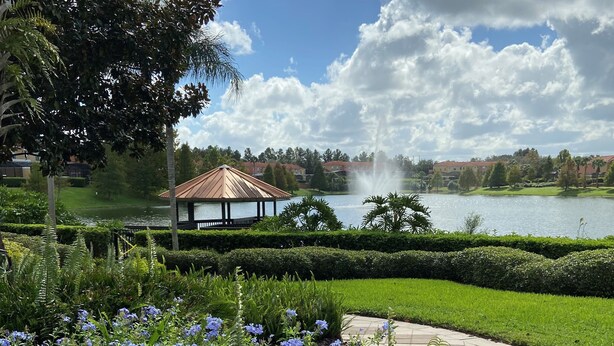 A gazebo with a tiled roof overlooking a lake, surrounded by lush greenery and a well-maintained garden with blue flowers. - The Encantada Escape – 3BR Townhome w/ Private Pool (Four Corners)