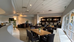 A modern dining area with a curved white reception desk, multiple tables and chairs, and a kitchen area in the background. - The Encantada Escape – 3BR Townhome w/ Private Pool (Four Corners)