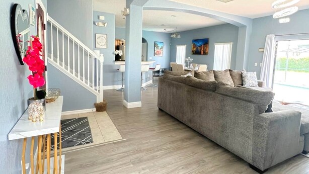 A spacious living area with a grey sofa, a dining table, and a staircase leading to another level.