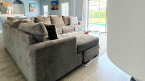 A modern living room with a sectional sofa, a glass coffee table, and a view of a pool through large windows.