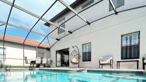 A swimming pool with a clear blue water surface, surrounded by a covered patio area with chairs and tables.