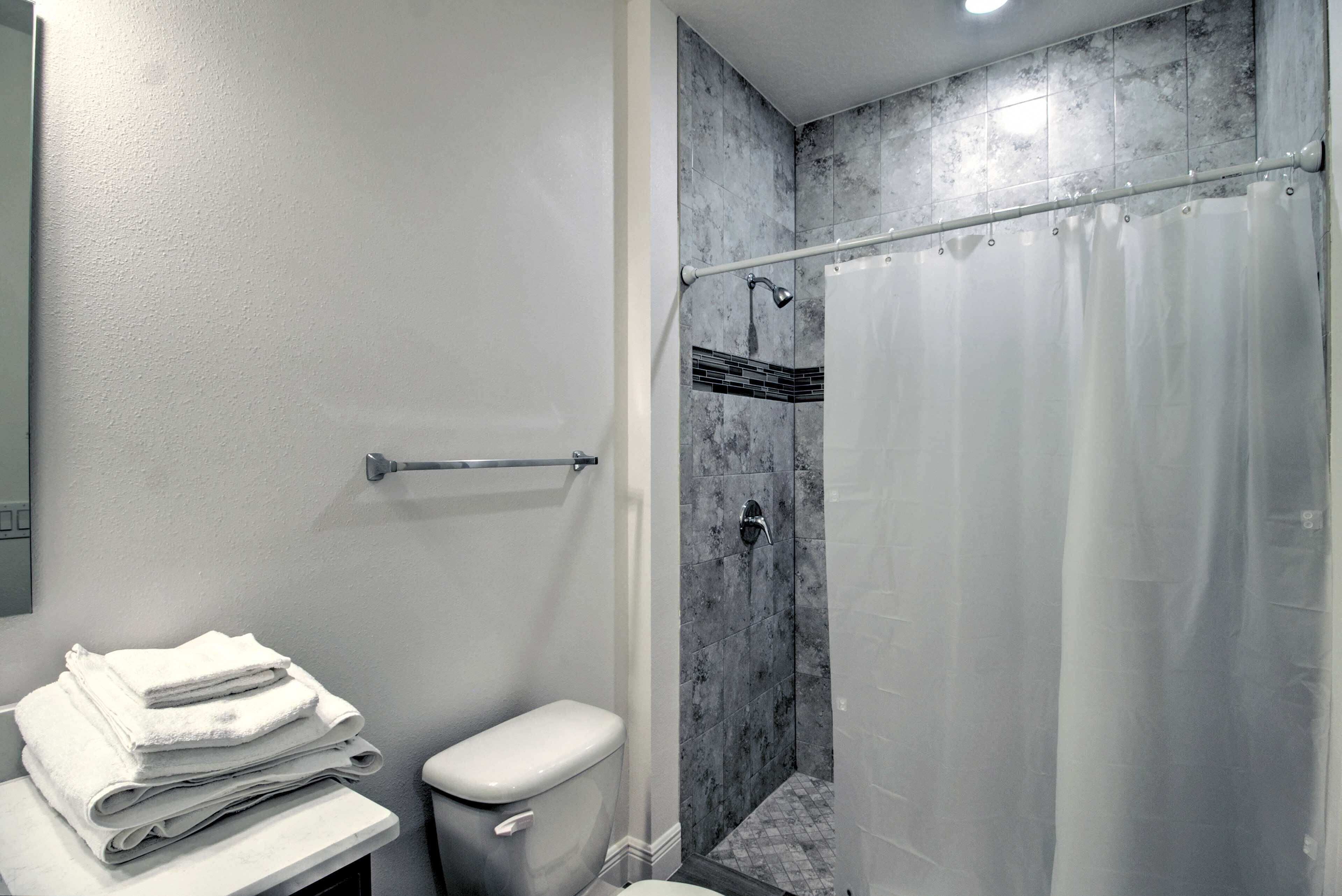 Un baño con inodoro, una pila de toallas blancas, ducha con puerta de vidrio y pared de mármol.