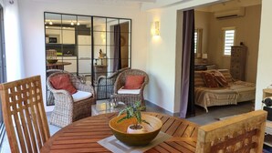 Un área de estar acogedora con muebles de mimbre, una mesa redonda de madera con un cuenco y una planta, y vistas a una cocina.