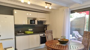 Una cocina moderna con armarios blancos, un microondas y un lavabo. Hay una mesa redonda de madera con sillas y un cuenco de fruta.