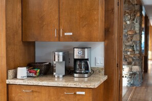 Een keuken met houten kastjes, een koffiezetapparaat, een koffiekan en een mand met koffiecups.