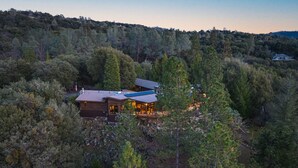 Una cabaña aislada rodeada de un bosque denso, con una terraza amplia y una chimenea destacada.