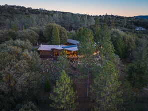 A secluded cabin surrounded by dense forest, featuring a large deck and a prominent chimney. - Mountain Oasis, Sleeps 24, Hot tub, Game room (Oakhurst)